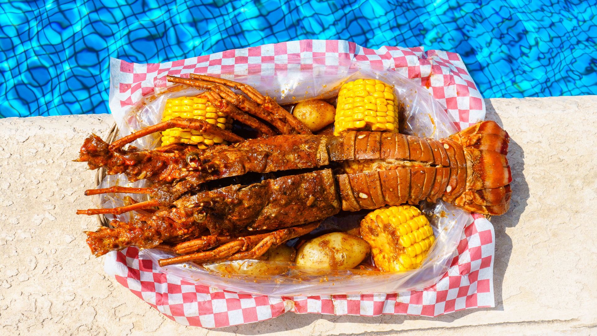 Close-up of a flavorful lobster with corn and potatoes by a poolside.
